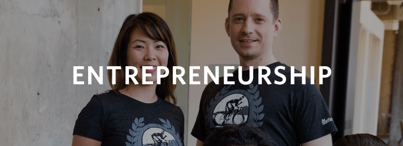 A group of people wearing matching t-shirts with a logo, overlaid with the word "ENTREPRENEURSHIP" in bold white letters.