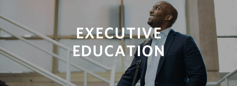 A person in a suit is standing in an office-like environment, looking upward and smiling, with the text "Executive Education" overlaid.